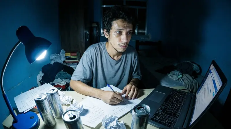 Rapaz de madrugada na mesa, olhos arregalados, cercado de latas de energético