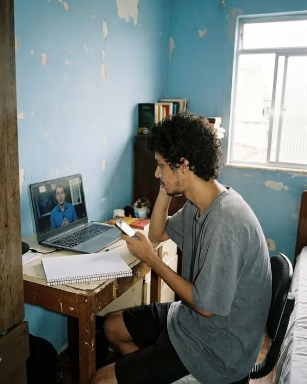 Rapaz na mesa com caderno aberto, vendo vídeo no notebook